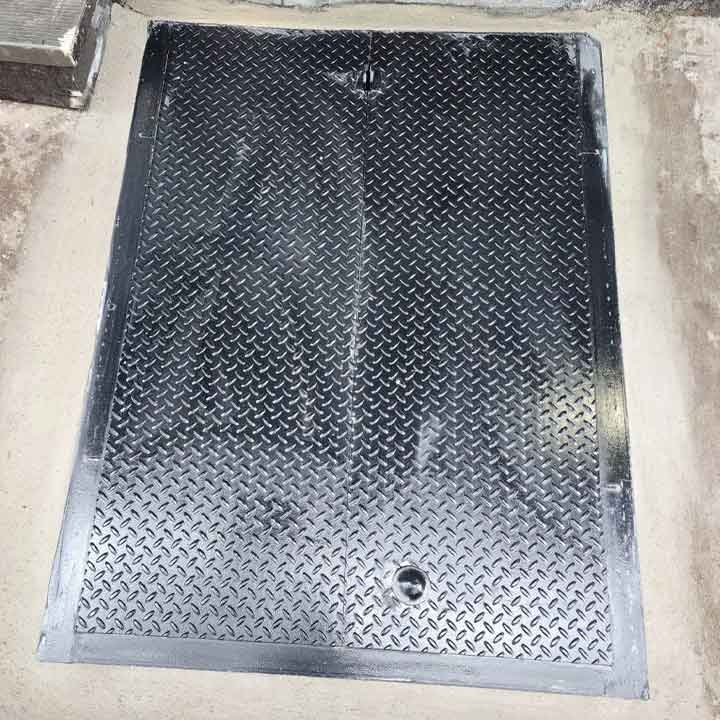 Newly installed black steel cellar hatch door closed flush with tiled outdoor floor, featuring diamond plate surface and secure fit.